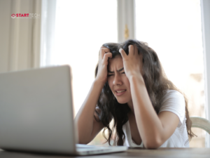 Woman has head in hands looking at laptop