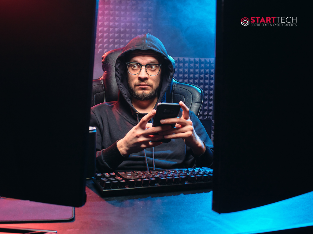 A hacker in front of two computers, holding a phone